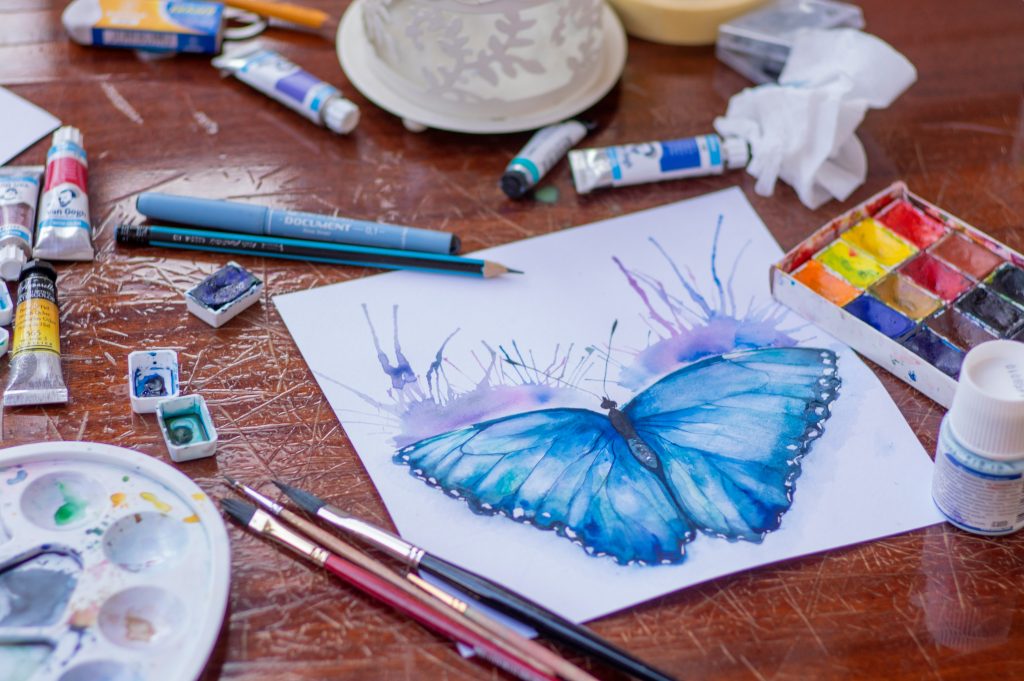 a table with art supplies and a picture of a watercolor butterfly